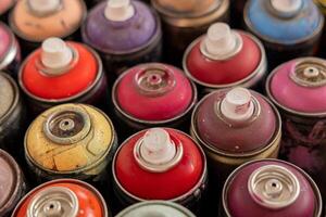 A closeup view of various colorful spray paint cans, showcasing different vibrant shades and worn textures, ideal for artistic projects. photo
