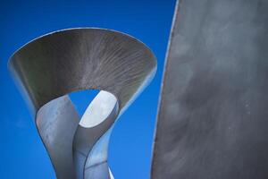 Abstract metal sculpture with twisting, open form against a bright blue sky. Smooth, reflective surface and dynamic curves. photo