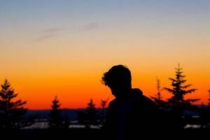 Young man silhouette on top of a mountain with a sunset in the background photo