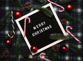 Merry Christmas lettering in plastic letters on an old vintage letter board. On the background there are caramel canes, balls, cones and fir branches. Top view. Flatley. Christmas greeting card. photo
