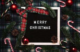 Merry Christmas lettering in plastic letters on an old vintage letter board. On the background there are caramel canes, balls, cones and fir branches. Top view. Flatley. Christmas greeting card. photo