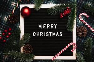 Merry Christmas lettering in plastic letters on an old vintage letter board. On the background there are caramel canes, balls, cones and fir branches. Top view. Flatley. Christmas greeting card. photo