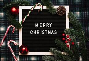 Merry Christmas lettering in plastic letters on an old vintage letter board. There are caramel canes, balls, cones and fir branches all around. Top view. Flatley. Ready-made Christmas greeting card. photo