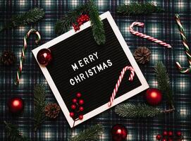 Merry Christmas lettering in plastic letters on an old vintage letter board. On the background there are caramel canes, balls, cones and fir branches. Top view. Flatley. Christmas greeting card. photo