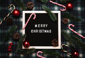 Merry Christmas lettering in plastic letters on an old vintage letter board. There are caramel canes, balls, cones and fir branches all around. Top view. Flatley. Ready-made Christmas greeting card. photo
