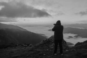 A man photographer taking a photo with dslr camera on the mountain top with nature background travel photography.