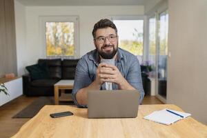 A smiling man using a laptop while working at home office. photo