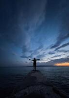 A happy free person standing alone with hands up and looking at the seashore concept of freedom. photo
