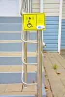 Yellow sign and call button outside of building with for people in wheelchair. Employee call button and braille text for blind people at the entrance to the drug store. Inclusive society photo