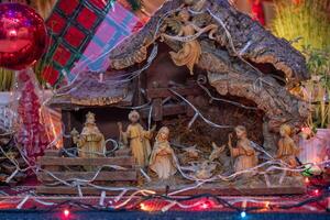 A traditional Nativity scene depicting the birth of Jesus, featuring figurines of Mary, Joseph, baby Jesus in a manger, shepherds, wise men, an angel, and animals, illuminated by festive lights photo