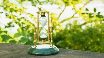 A golden hourglass sitting on a table in front of a river photo
