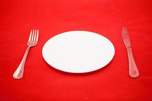 A white plate with a fork and knife on a red background photo