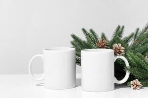 Christmas mockup white empty tea mugs on a white table and branches of a Christmas tree wreath. photo