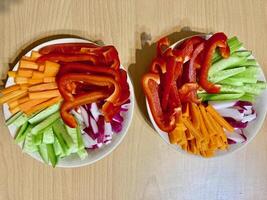 Two plates of healthy fresh snacks with sliced carrot, bell pepper, cucumber, and radish sticks are arranged on a light table photo