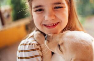 Close-up portrait of a little girl hugging a puppy. A cute small kid is playing with a dog. A sweet child is happy with her pet. photo