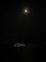 A boat is in the water at night with a full moon photo