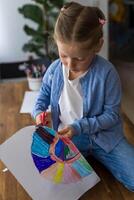 A young girl carefully cuts out her drawing with scissors, showcasing her creativity and focus. photo