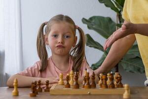 Smiling little girl plays chess with her grandmother at the table,enjoying loving and playful moment photo