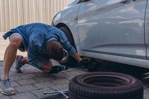 Young man in unscrewing lug nuts on car wheel in process of new tire replacement,using wrench while changing flat tire on the road. photo