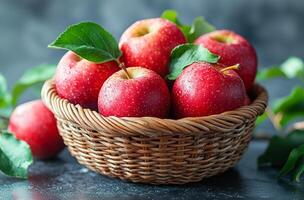 A basket of red apples with green leaves on top. The apples are shiny and wet, and the basket is made of woven material. Concept of freshness and abundance, as the apples are ripe photo