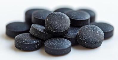A pile of black pills with a lot of white space between them. The pills are small and black, and they are piled on top of each other. Concept of organization and order photo