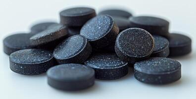 A pile of black pills on a white surface. The pills are small and round, and they are all the same color. Concept of uniformity and order, as the pills are neatly stacked on top of each other photo