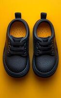 Two black shoes with yellow laces are placed on a yellow background. The shoes are made of leather and have a shiny appearance. The yellow laces contrast with the black shoes, making them stand out photo