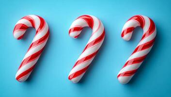 Three red and white candy canes are arranged on a blue background. The candy canes are placed in a row, with the middle one slightly overlapping the other two. The arrangement creates a festive photo