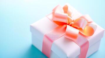 A white box with pink ribbon on top. The box is decorated with a bow and is sitting on a blue background photo