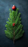 A Christmas tree made out of a single green branch with red berries on it. A red ornament is on top of the tree photo