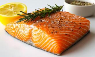 A piece of salmon with lemon and rosemary on top. The salmon is cut into a diamond shape and is sitting on a white plate photo