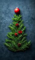 A Christmas tree made of pine needles and red berries. The tree is on a dark background. The tree is decorated with a red ball on top photo