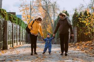 A loving couple strolls through a sunlit park with their young son, surrounded by the vibrant colors of autumn, enjoying a joyful and peaceful family moment together. photo