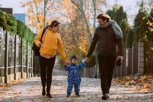 A loving couple strolls through a sunlit park with their young son, surrounded by the vibrant colors of autumn, enjoying a joyful and peaceful family moment together. photo
