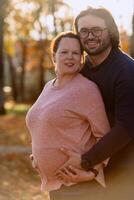 A man lovingly embraces his pregnant wife in the park, sharing a peaceful moment of warmth and affection photo