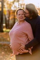 A man lovingly embraces his pregnant wife in the park, sharing a peaceful moment of warmth and affection photo