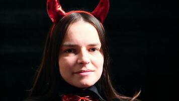 Young brunette woman with red horns and butterfly on her neck embodies devilish charm, portraying devil with captivating smile Her playful look adds intrigue, making her devil character unforgettable. video