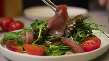 Process of preparing delicious Caesar salad with bacon involves chef spreading thinly-sliced pieces of fresh, cooked bacon over bed of vegetables and herbs. video