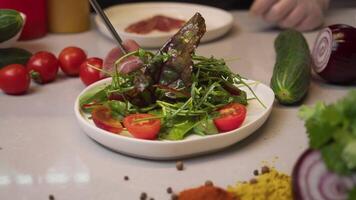 Process of preparing delectable Caesar salad with bacon entails chef spreading thinly-sliced pieces of freshly cooked bacon over bed of vegetables and herbs. video