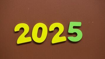 Stop motion sequence showing the colorful numbers 2025 with yellow and green digits arranged on a brown textured background video