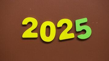 Stop motion sequence showing the colorful numbers 2025 with yellow and green digits arranged on a brown textured background video