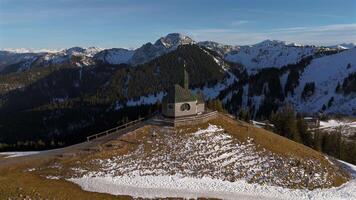 Kapelle Heilig Kreuz Rottach-Egern Tegernsee. Wallbergkapelle on mountain Wallberg overlooking lake Tegernsee and mountain range in sunny spring weather with snow at sunset. Chapel on peak of Alps. video