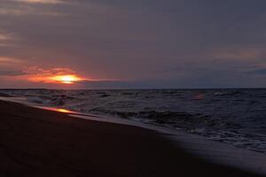 The sun sets slowly over the ocean, casting a warm glow on the sandy beach while gentle waves lap at the shore photo