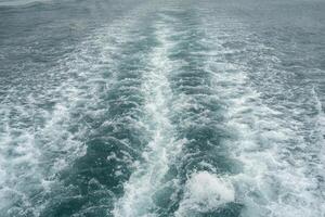 Rippling waves create dynamic patterns behind a boat as it moves through a serene sea under an overcast sky photo
