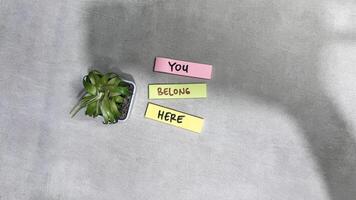 Concept of You Belong Here write on sticky notes isolated on Wooden Table. photo