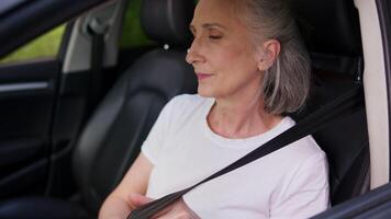 Satisfied Caucasian elderly aged senior woman female mature car driver auto owner grandmother rental service client sitting inside new automobile fastens seat belt safety vehicle transport protection video