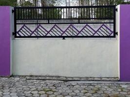 A modern fence with a purple accent wall and pillars. The fence features a geometric design and is situated in front of a bamboo grove. photo