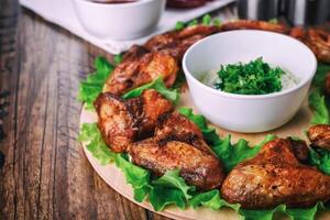 delicious grilled chicken wings with garlic and tomato sauce with lettuce on a round board on wooden rustic background photo