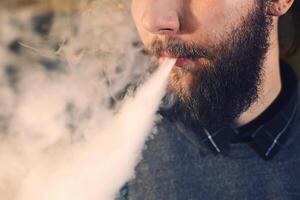 Men with beard vaping and releases a cloud of vapor. close-up. photo