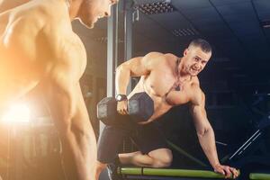 power athletic guy , execute exercise press with dumbbells, in sport hall photo